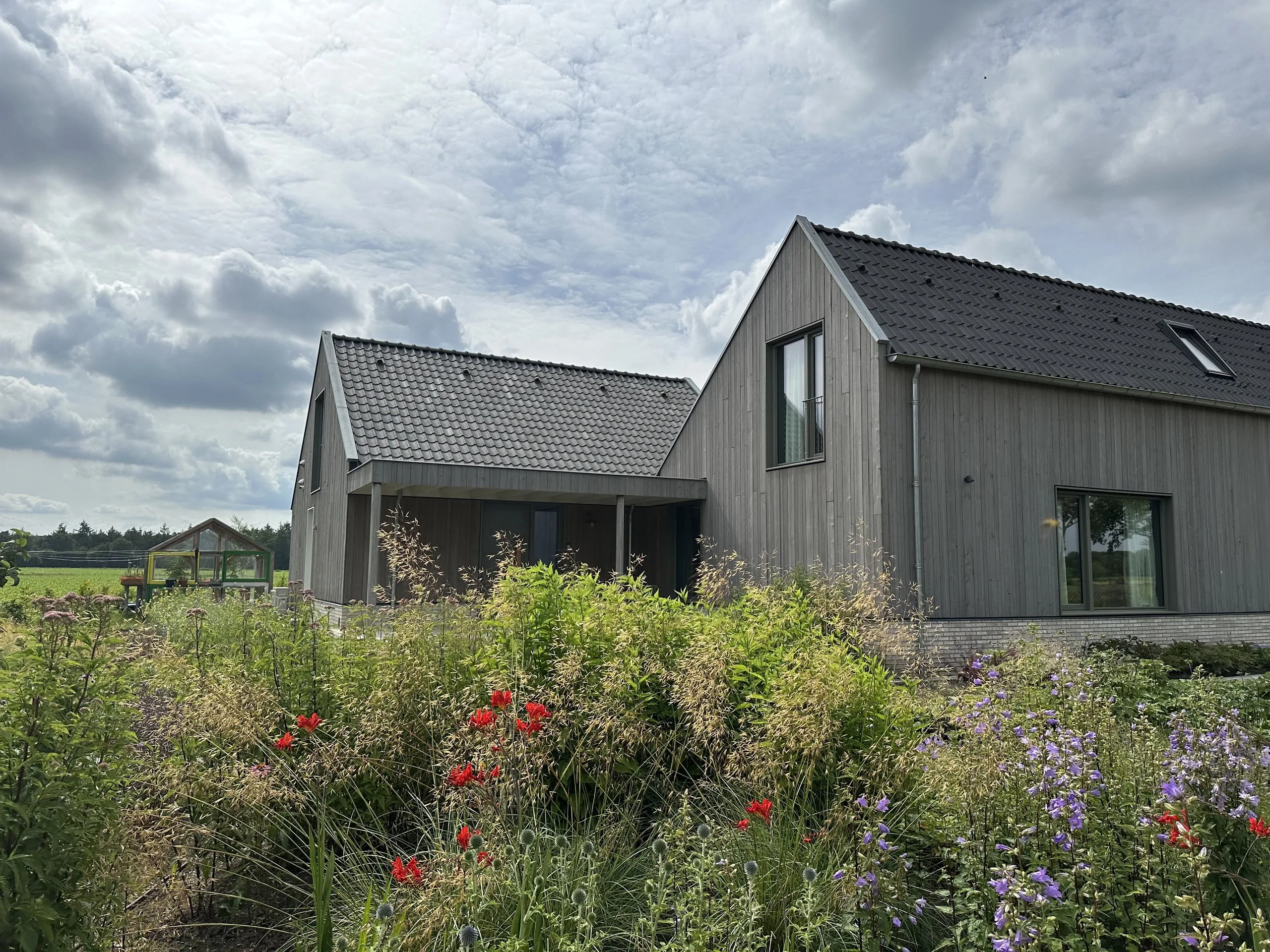 Woning met vergrijsde houten gevelbekleding achter een bloeiende tuin